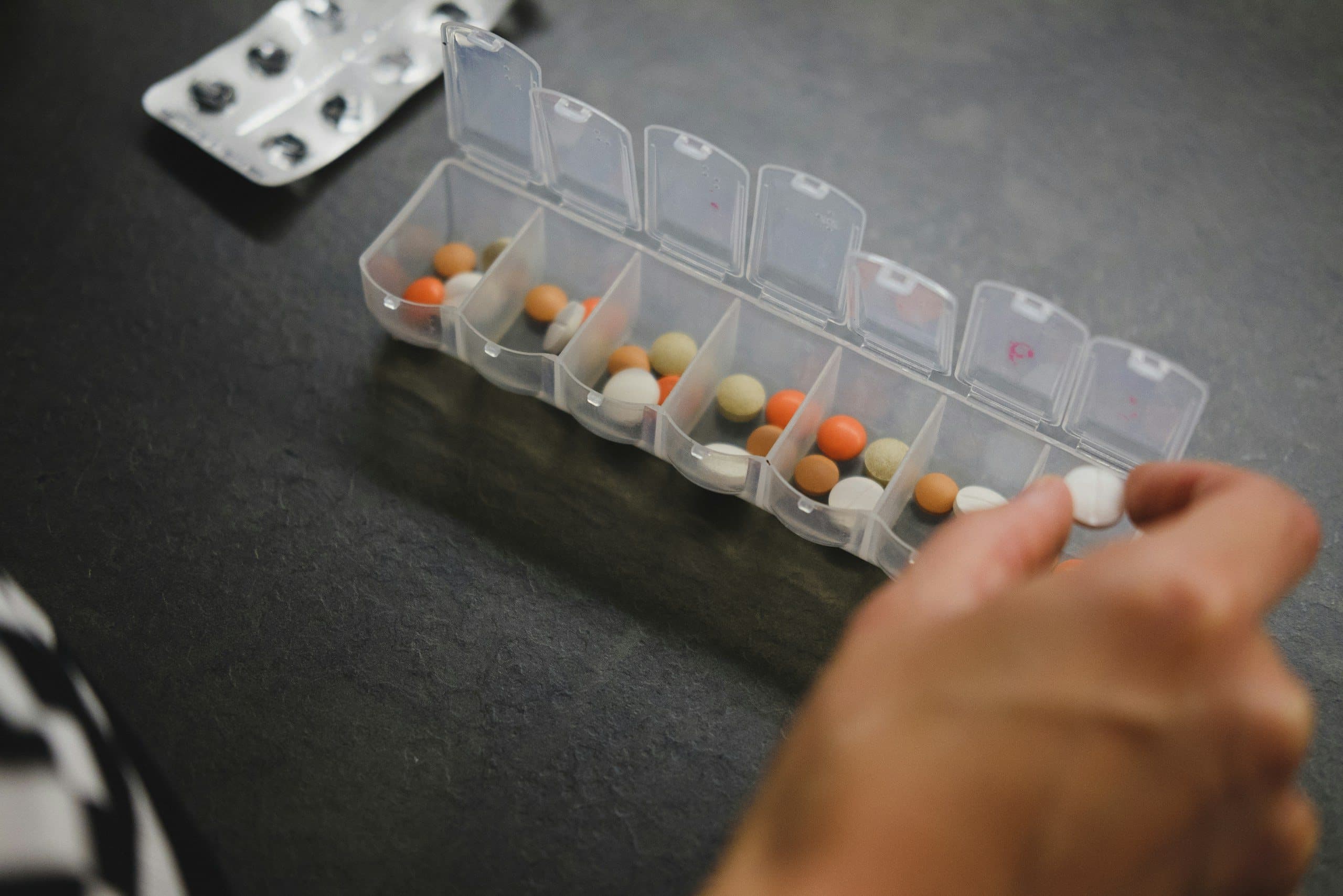 Weekly pill organizer being filled with refilled medication